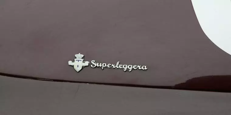Dettaglio del fregio metallico Superleggera con stemma della Carrozzeria Touring sulla scocca amaranto.