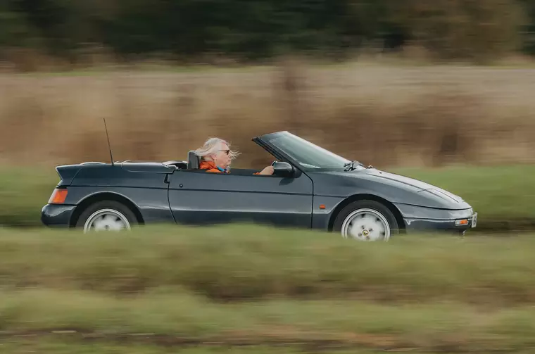 Lotus Elan M100 grigia scura aperta in azione dinamica su strada di campagna.