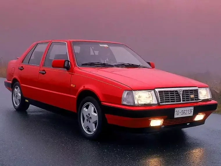 Lancia Thema 8.32 di colore rosso con fari accesi in un'atmosfera nebbiosa